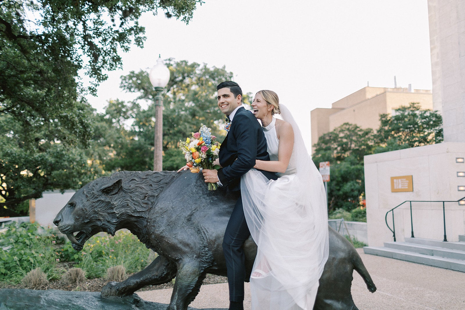 Bride and groom laugh on a statue in front of the museum