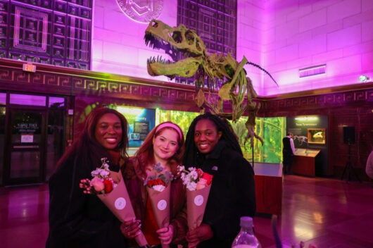 three young women holding flowers at Fossils & Flowers event in museum Great Hall